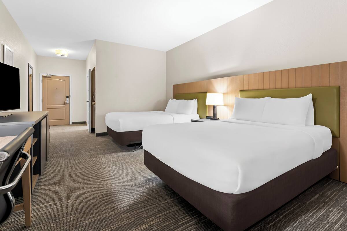 A hotel room with two beds, a desk, and a television.