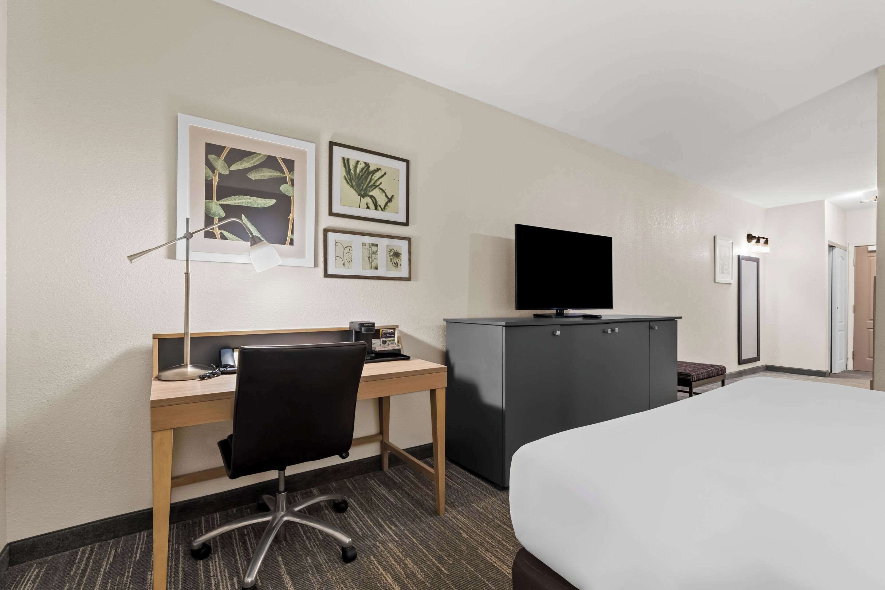 Habitación de hotel con cama, escritorio con silla, televisor, armario y cuadros en la pared.