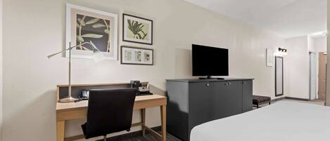 Habitación de hotel con cama, escritorio con silla, televisor, armario y cuadros en la pared.