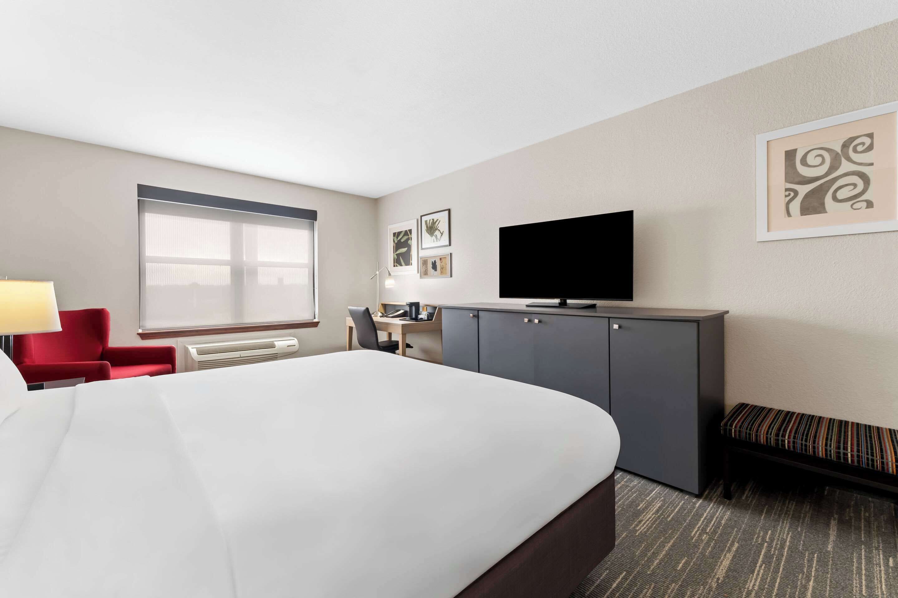 A hotel room with a large bed, a desk with a chair, a TV, and a window.