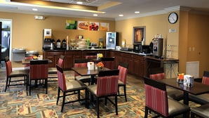 Een ontbijtruimte van een hotel met een balie, koffieautomaten en zitplaatsen.