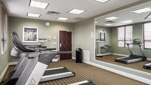 Een fitnessruimte met loopbanden, een spiegelwand en een klok aan de muur.