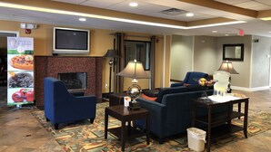 Een hotel lobby met een televisie, zithoek en een etalage met eten.