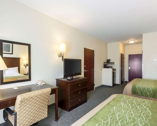 A hotel room with a bed, a desk with a chair, a television, a dresser, a mirror, and a door leading to another room.