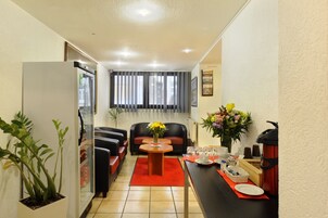 Un espacio habitable compacto con kitchenette, comedor y zona de estar con sofá y mesa de centro.