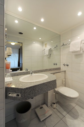 Un baño moderno con lavamanos de granito, un espejo grande, un inodoro y un cubo de basura.