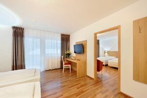 Habitación de hotel con piso de madera, un escritorio con silla, televisor, cama y armario.