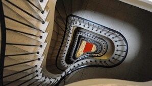 Uma escadaria em espiral com corrimãos de metal e um painel decorativo central vermelho e amarelo.