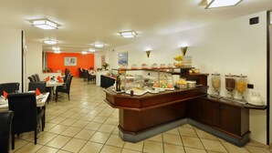 Uma área de buffet com diversas opções de comida, um espaço de estar com mesas e cadeiras, e uma parede de destaque em laranja vibrante.