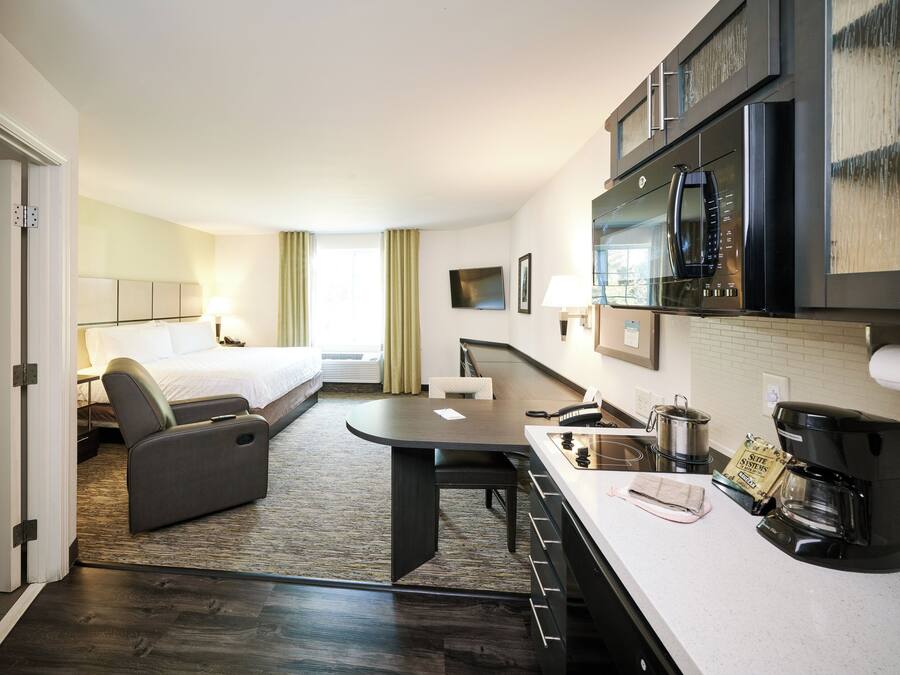 Ein Hotelzimmer mit Bett, Sofa, Esstisch, Mikrowelle, Kaffeemaschine und Fernseher.