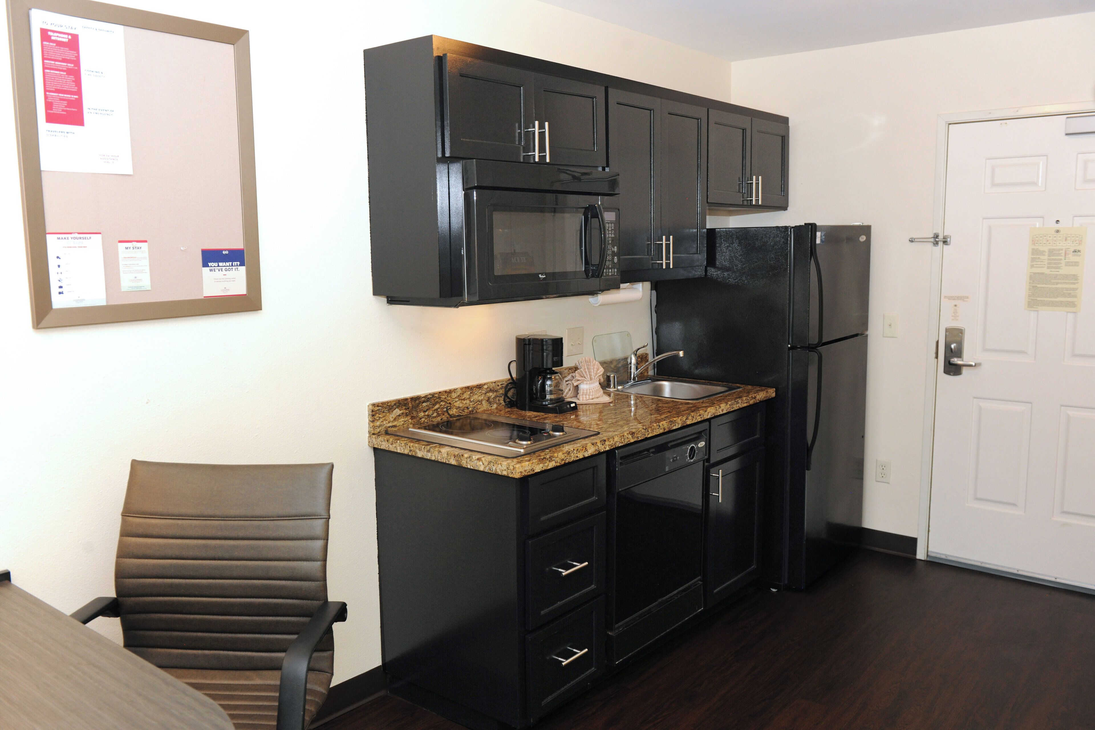 A compact kitchen with black cabinets, a microwave, a refrigerator, a sink, and a chair.