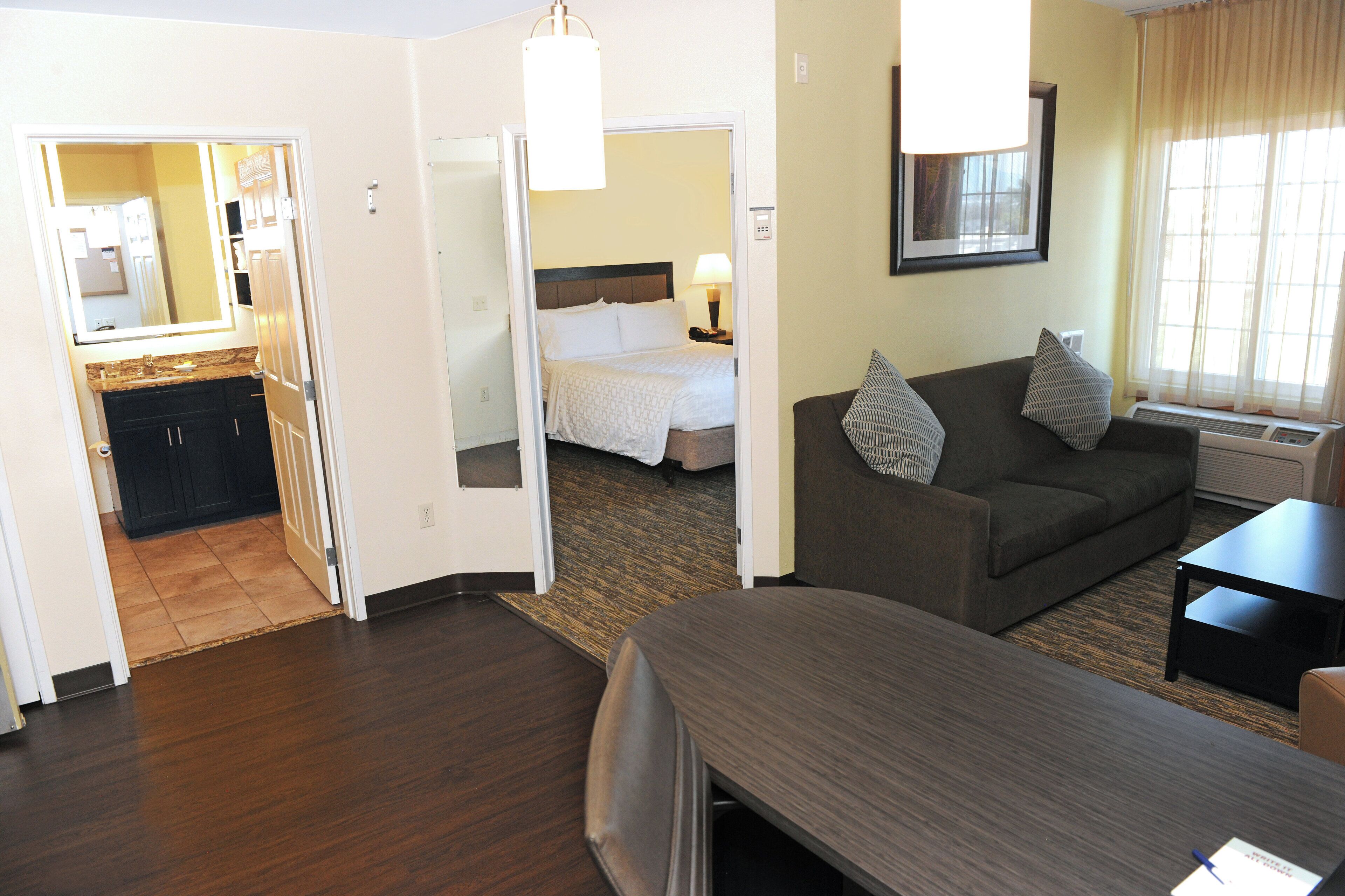 A hotel room with a bed, a sofa, a desk, and a bathroom visible through an open door.