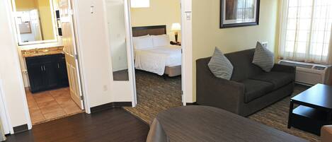 A hotel room with a bed, a sofa, a desk, and a bathroom visible through an open door.