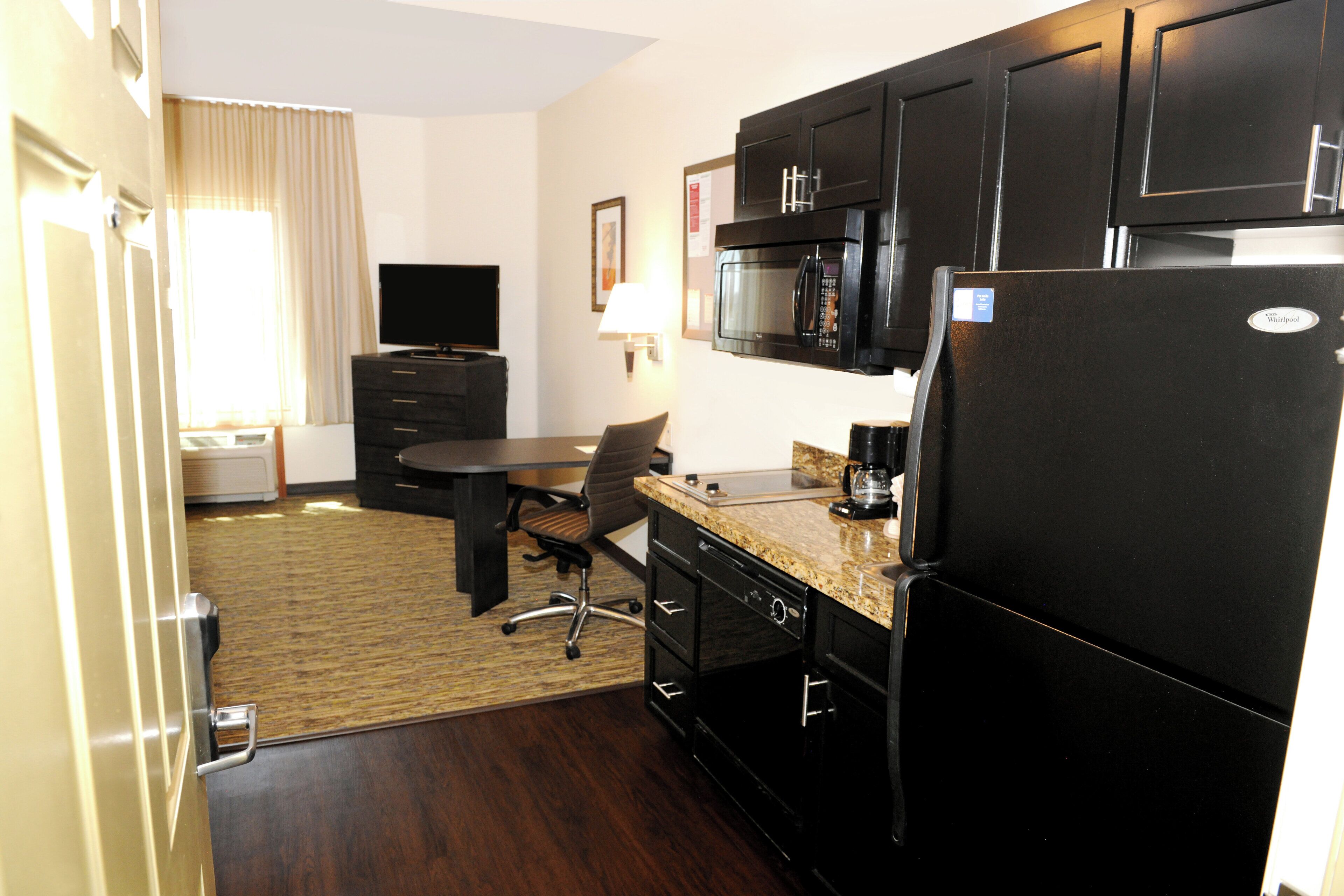 A compact hotel room with a kitchenette, a dining area, and a television.
