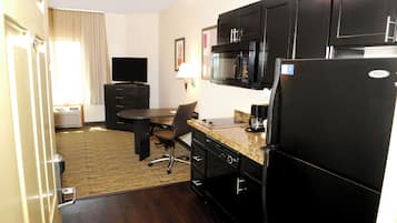 A compact hotel room with a kitchenette, a dining area, and a television.