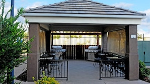 Un patio extérieur couvert, équipé de deux barbecues, doté d’un sol en béton et entouré d’une clôture en métal.