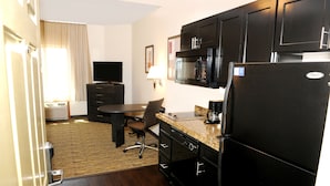 Une chambre d’hôtel compacte dotée d’une kitchenette, d’un coin repas, d’un téléviseur à écran plat et d’une fenêtre avec des rideaux.