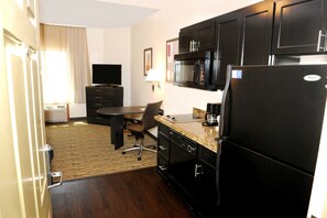 Ein kompaktes Hotelzimmer mit einer Küchenzeile, einem Essbereich, einem Flachbildfernseher und einem Fenster mit Vorhängen.