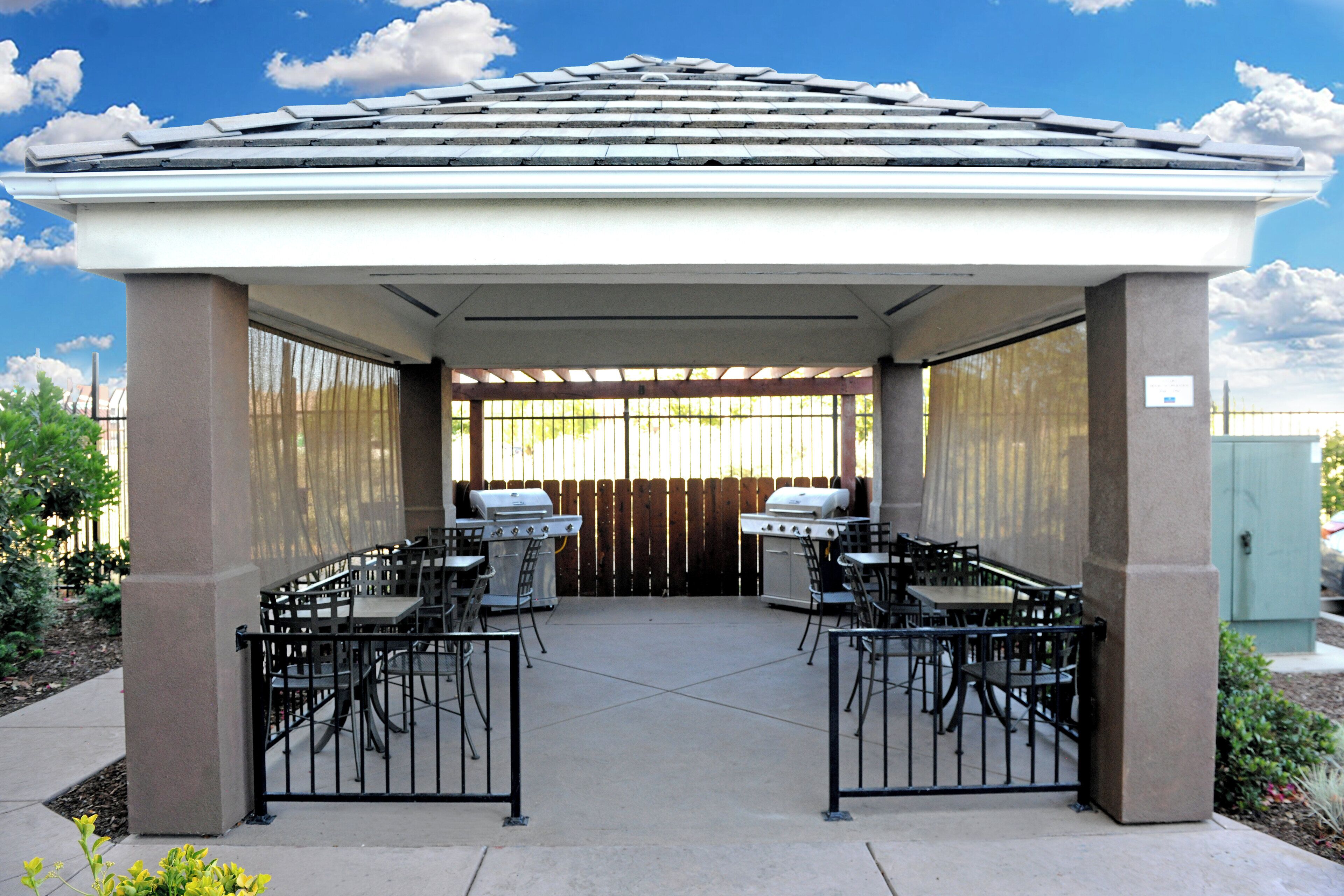 A covered patio area with two barbecue grills, tables, and chairs.
