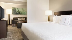 Ein Hotelzimmer mit einem großen Bett, einer Couch, einem Fernseher und einem Gemälde an der Wand.
