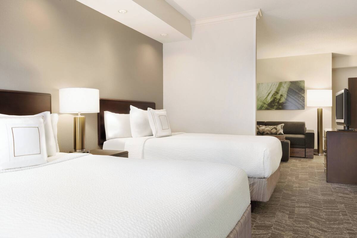 A hotel room with two beds, a desk, a television, and a painting on the wall.