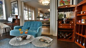 A living room with a blue armchair, two glass coffee tables with magazines, a wine rack, and a laptop on a desk. - Hôtel Escale Oceania Lorient (Lorient)