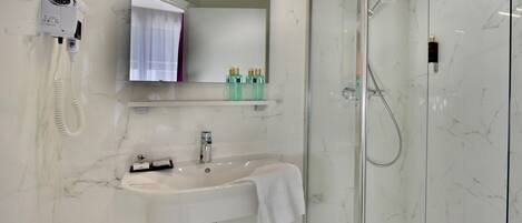 A modern bathroom with a marble sink, a handheld hair dryer, a glass-enclosed shower, and a mirror with a towel hanging on it.