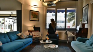 A modern living room with a blue sofa, a round coffee table, and a view of the outside through large windows. - Hôtel Escale Oceania Lorient (Lorient)