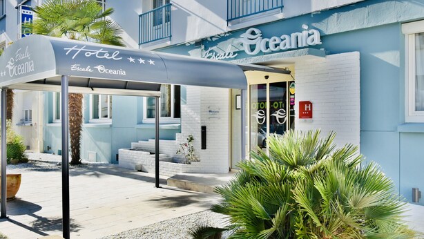 A hotel named 'Escale Oceania' with a covered entrance, white brick facade, and palm trees. - Hôtel Escale Oceania Lorient (Lorient)