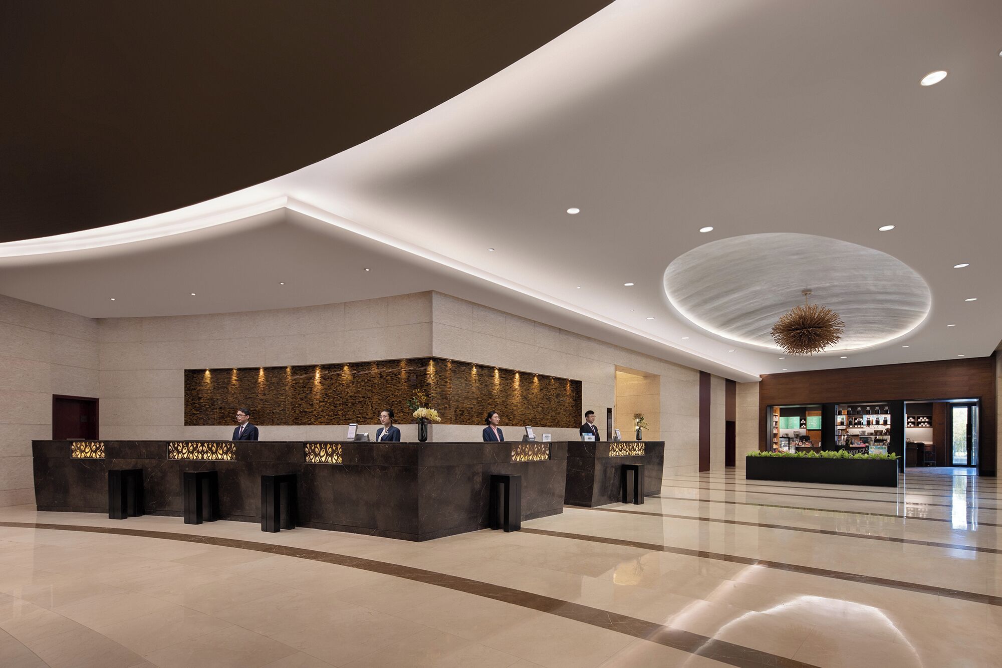 A modern hotel lobby with a reception desk, a large chandelier, and a view of the lobby area.