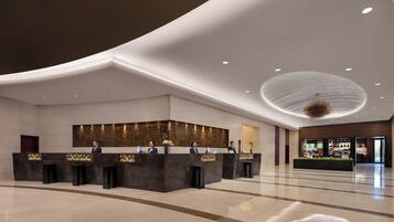 A modern hotel lobby with a reception desk, a large chandelier, and a view of the lobby area.