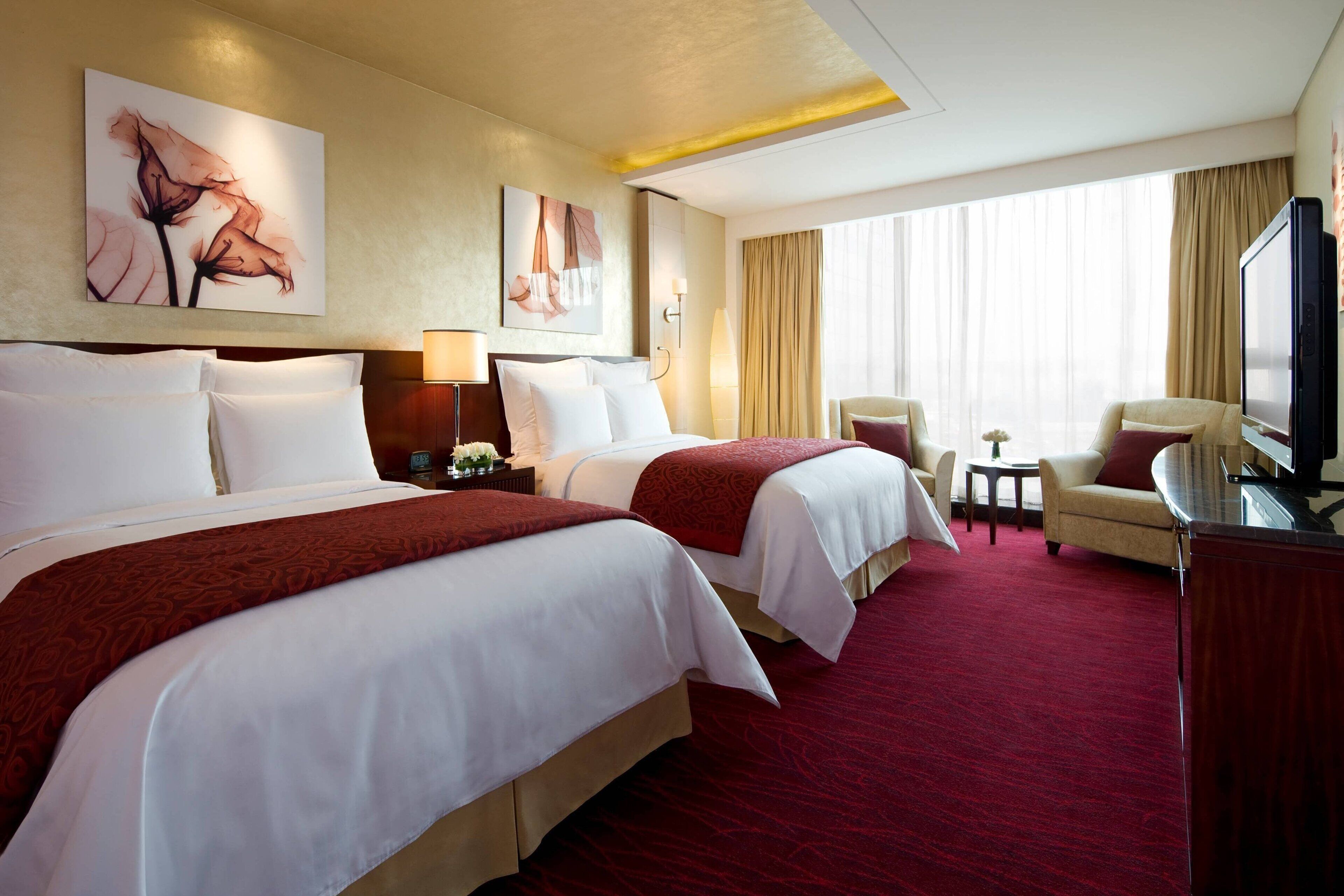 A hotel room with two beds, a TV, a desk, and a chair.