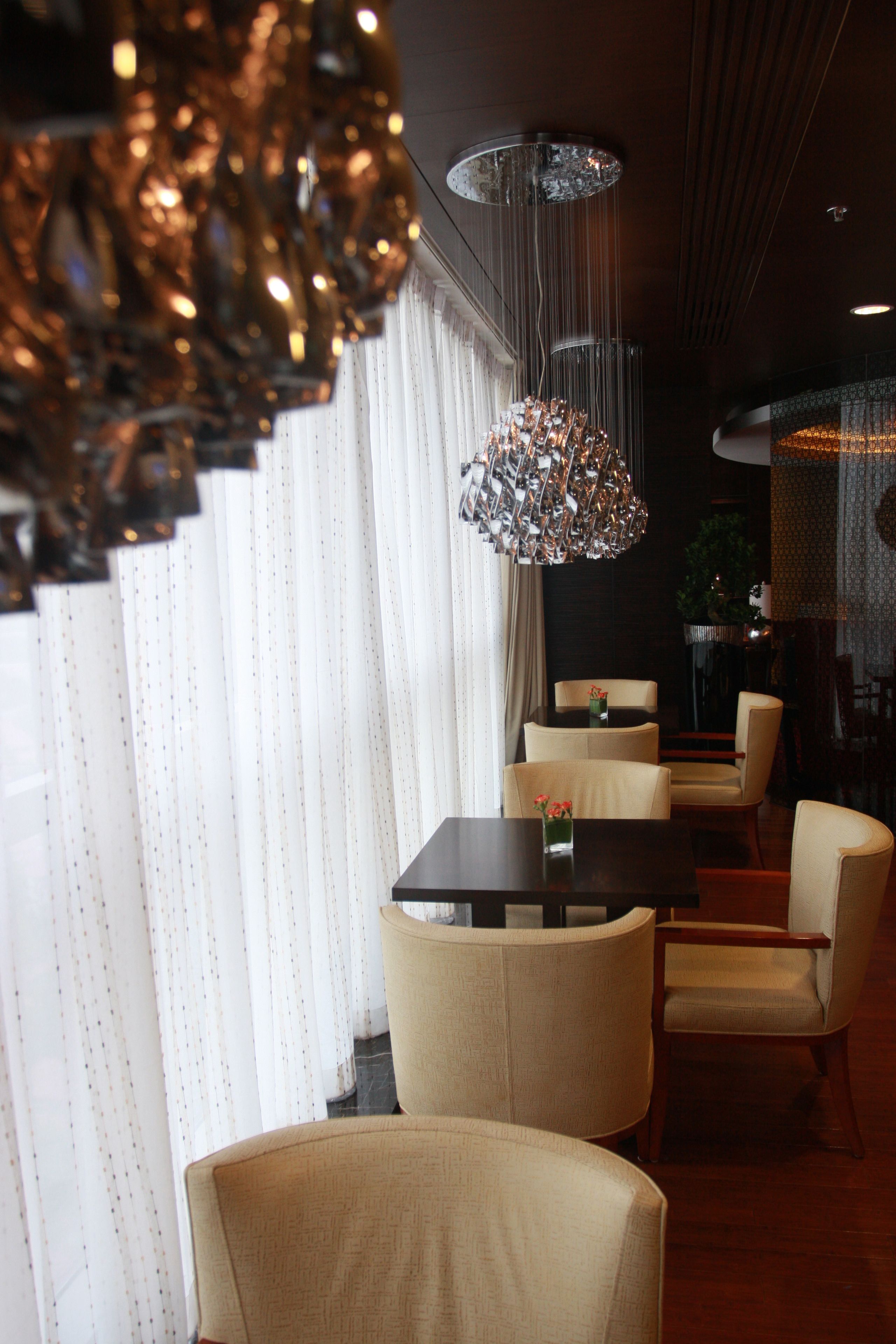 A dining area with a long table and multiple chairs, a hanging chandelier, and a patterned curtain in the background.
