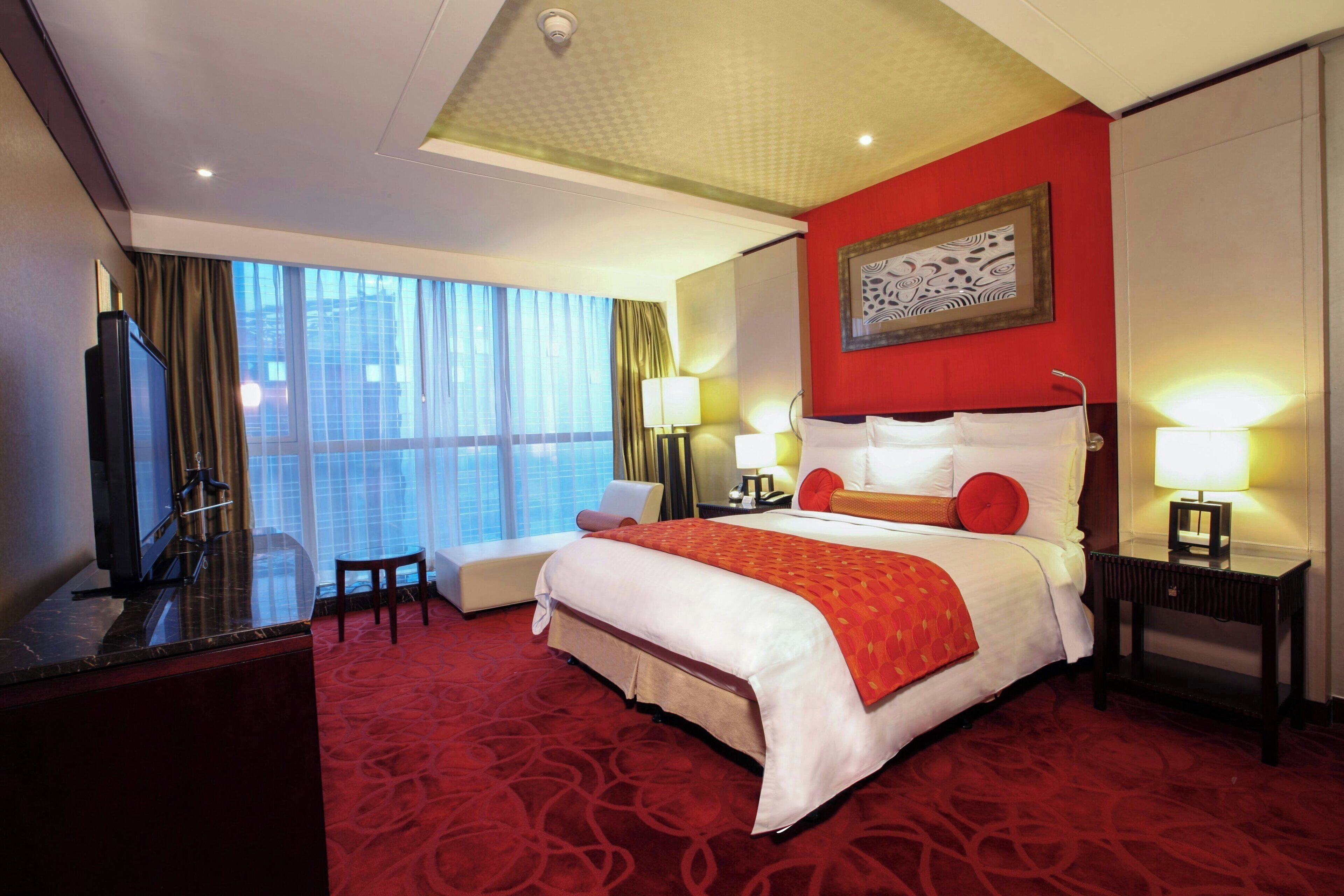 A hotel room with a large bed, a desk, a chair, a TV, and a window with curtains.