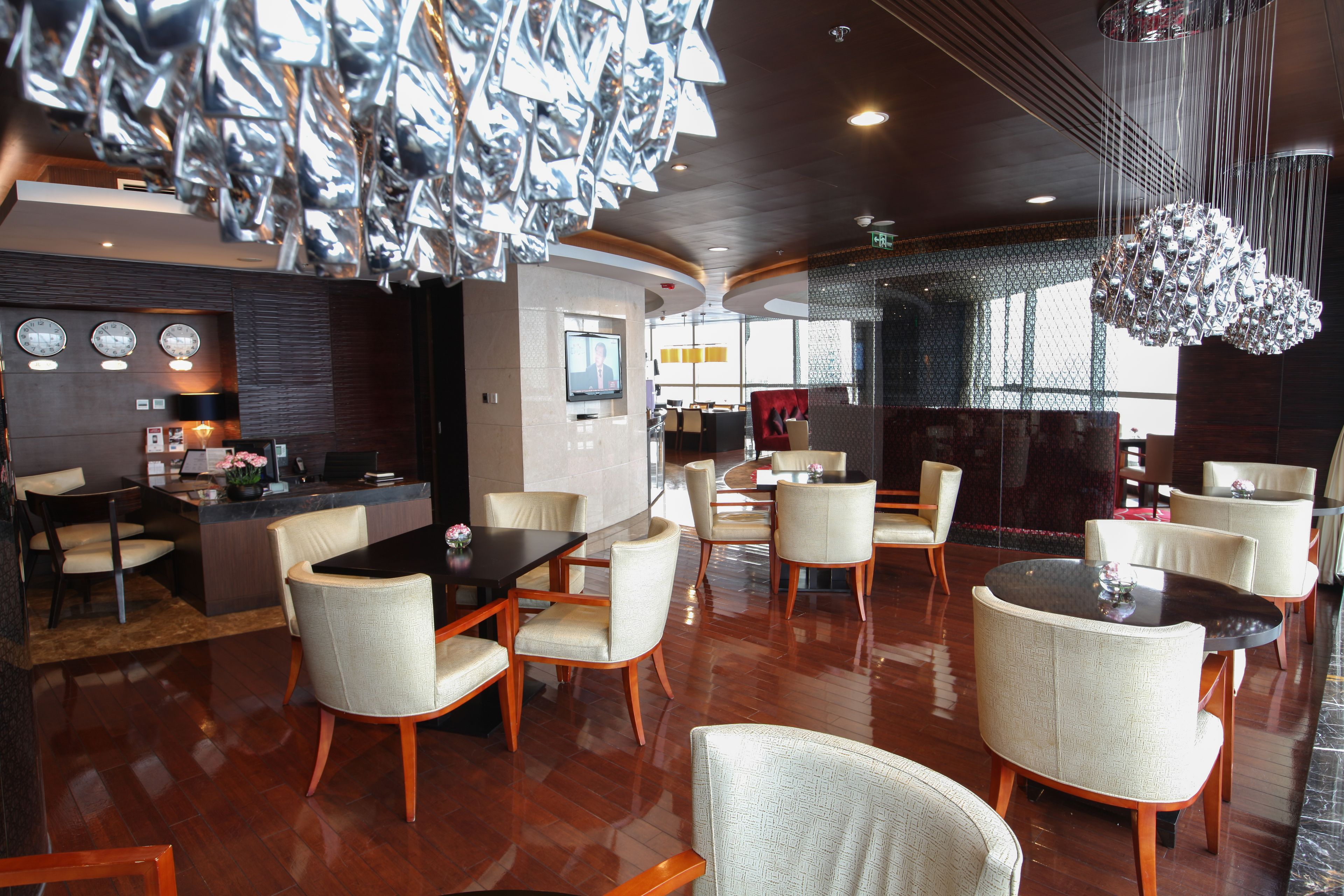 A modern hotel lobby with a central dining area, a reception desk, and a large chandelier.