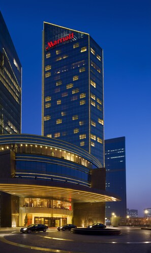 A Marriott hotel with a modern glass facade, illuminated windows, and a curved entrance with a well-lit driveway. - Beijing Marriott Hotel Northeast (Beijing)