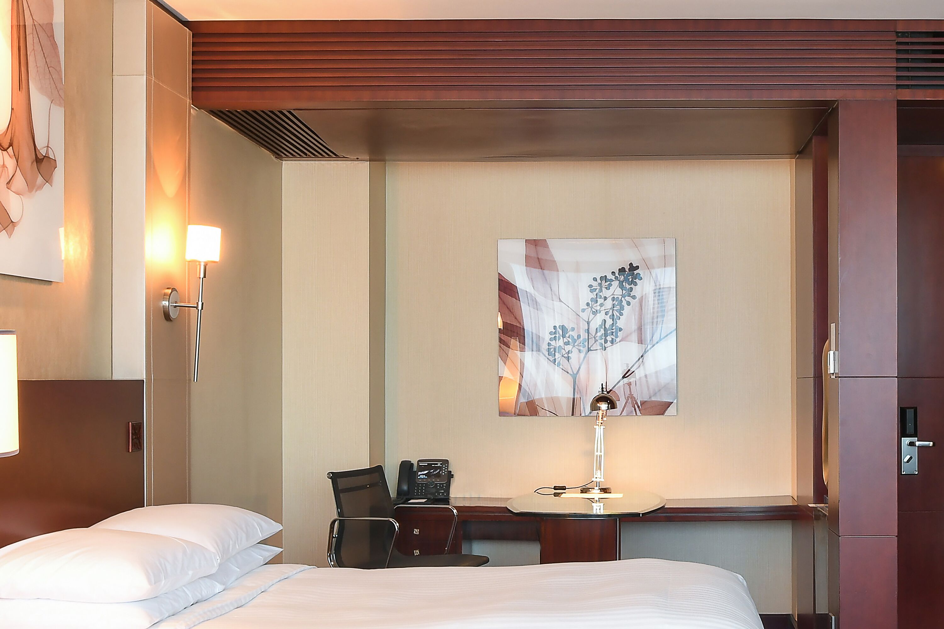 A hotel room with a bed, a desk with a telephone, a lamp, and a painting on the wall.