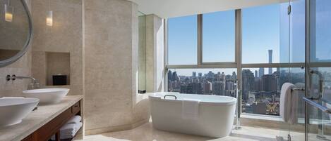 A modern bathroom with two sinks, a freestanding bathtub, and a large window offering a city view.