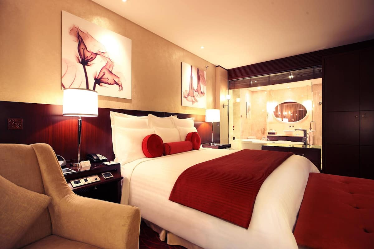 A hotel room with a large bed, a bedside table with a lamp, a chair, and artwork on the walls.