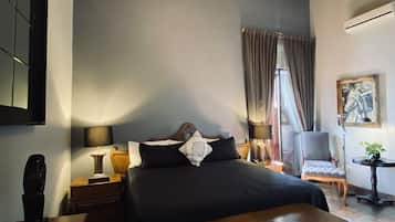 A modern bedroom with a wooden ceiling, a large bed, a nightstand, a chair, and a small table with a plant.