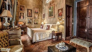 A traditional room with a bed, a chair, a table, and a bench. There are pictures on the walls and a chandelier. - Casa Pedro Loza (Guadalajara)