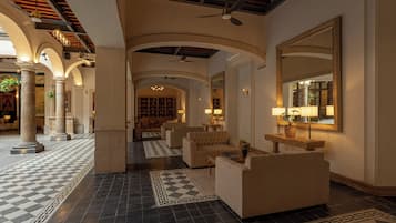Un hall espacioso con suelo a cuadros, una zona de estar con sofás, un espejo grande y un ventilador de techo.