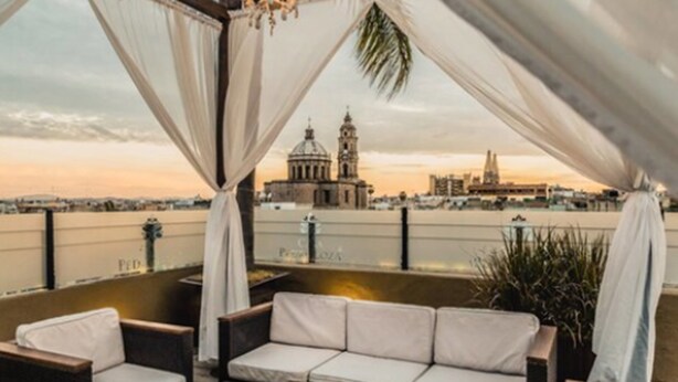 A rooftop terrace with a sofa and chairs, overlooking a cityscape with a prominent building and a bridge. - Casa Pedro Loza (Guadalajara)