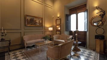 A room with a checkered floor, a sofa, a chair, a table with a plant, and a painting on the wall.