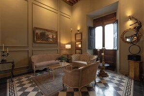 Una habitación con piso a cuadros, un sofá, una silla, una mesa con una planta y un cuadro en la pared.
