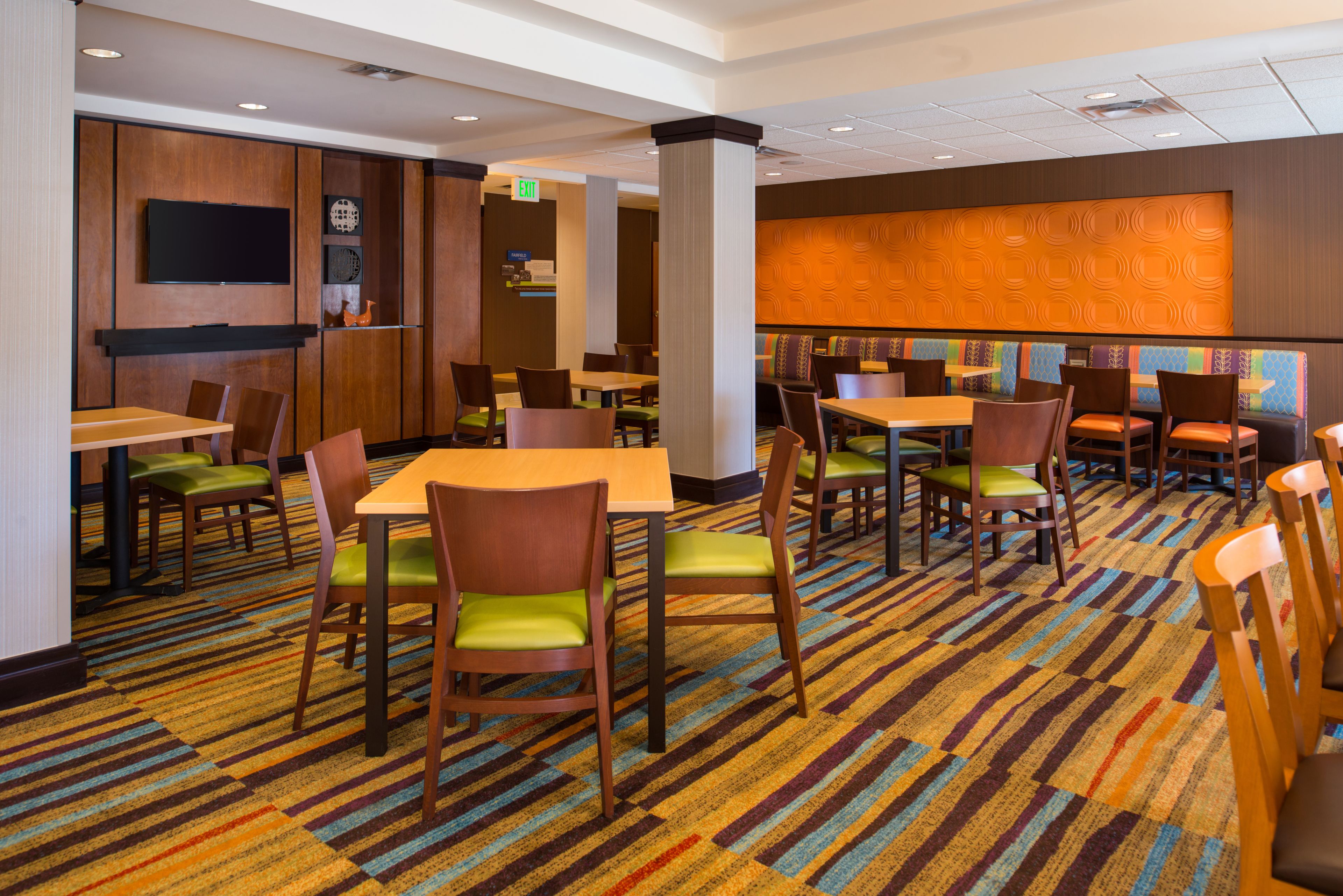 Een restaurantgedeelte in een hotel, met meerdere tafels en stoelen, een wandtelevisie en een vloerbedekking.