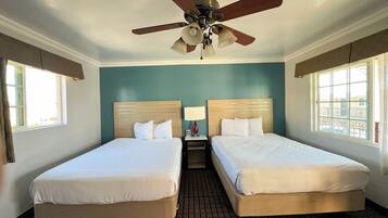 A hotel room with two single beds, a ceiling fan, a nightstand with a lamp, and a window with a view.
