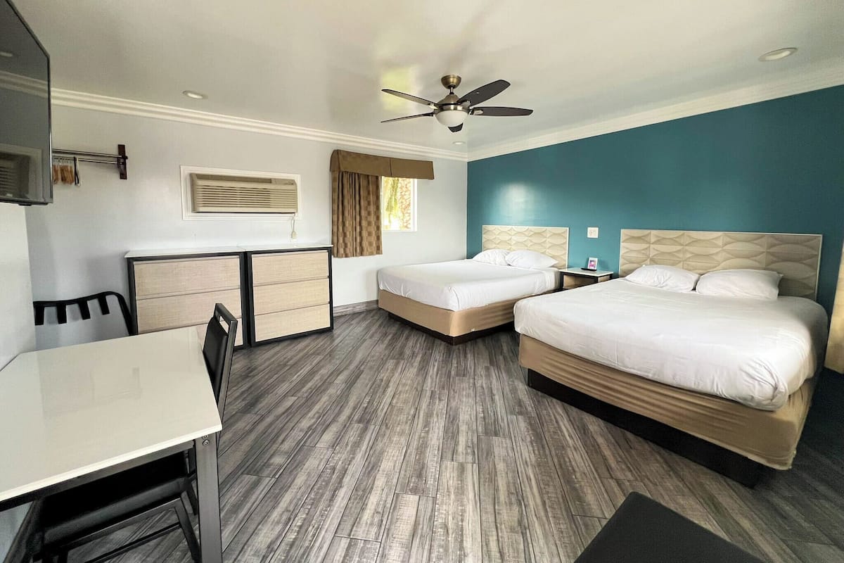 A hotel room with two beds, a desk, a chair, a ceiling fan, and a window with curtains.