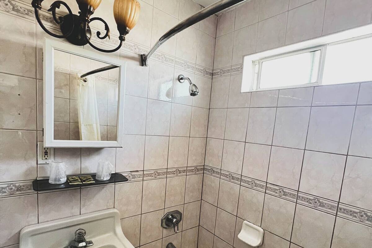 A bathroom with a bathtub, a sink, a showerhead, and a wall-mounted light fixture.