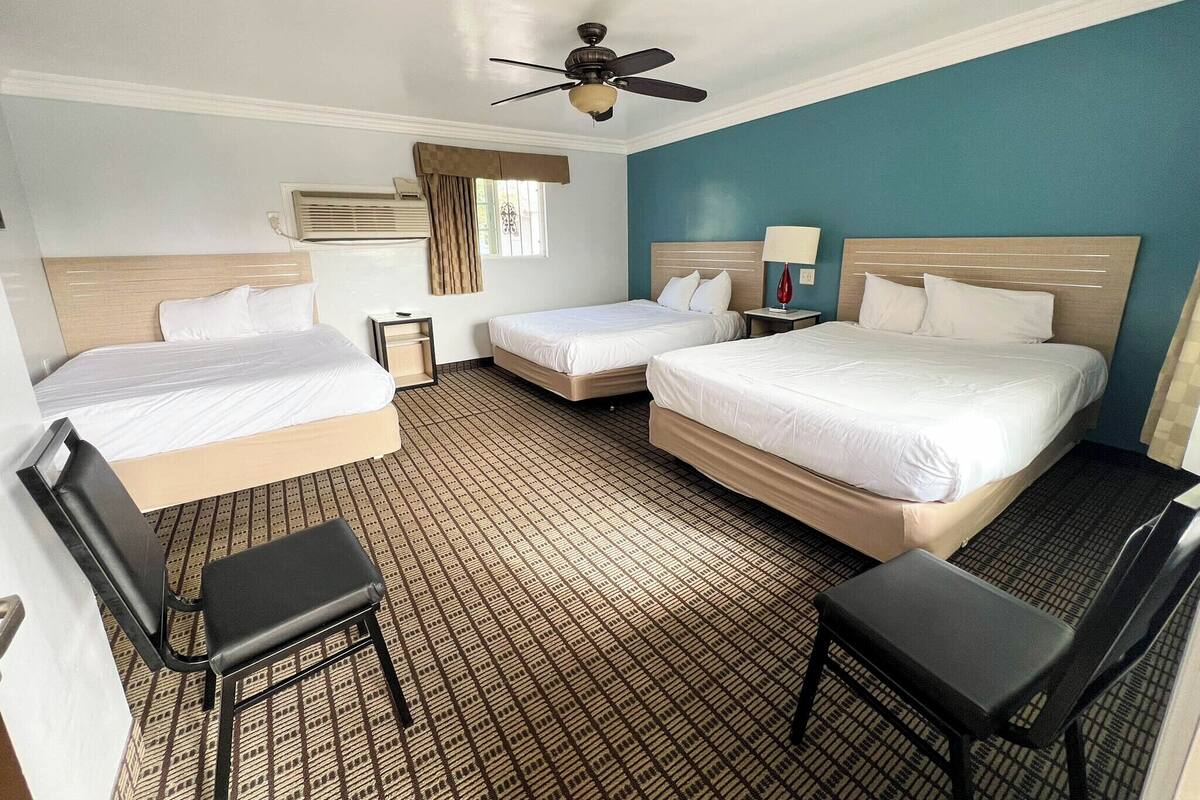 A hotel room with two single beds, a double bed, a ceiling fan, a window with curtains, a desk, and a chair.